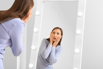 Displeased young woman looking in mirror at home