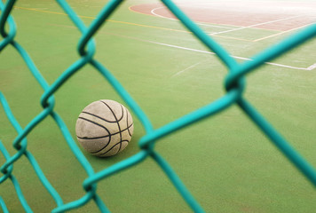 An old, used, dirty basketball behind a wire fence; on a basketball field; inside a school.
