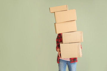 Asian man with moving boxes on color background