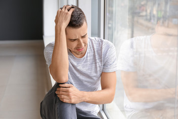 Depressed young man near window