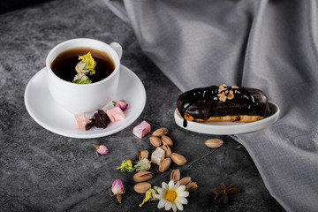Obraz na płótnie Canvas A cup of tea with Turkish lokum, pistachios and chocolate eclair.