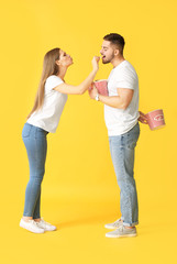 Emotional young couple with popcorn on color background