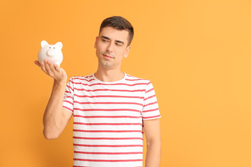 Thoughtful man with piggy bank on color background