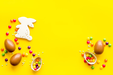 Sweet Easter symbols - chocolate eggs and bunny gingerbread - on yellow background top-down frame copy space