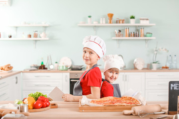 Cute little chefs with cook books in kitchen