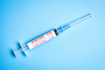 Obraz premium Medical syringe with the inscription COVID-19 on a blue background. Virus epidemic concept.