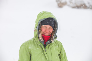 girl with hoarfrosted hair in green jacket grey hat and with red scarf in Caucasus mountains