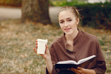 Beautiful girl studies. Student use the notebook. Lady in a summer park. Girl with cup of coffee