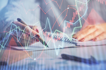 Double exposure of woman's hands making notes with forex graph hologram. Concept stock market analysis.