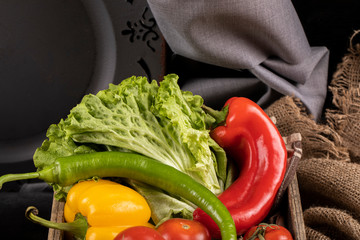 Colorful hot chili peppers and green lettuce leaves in a rustic wooden tray