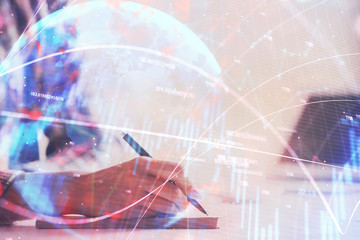 Fototapeta na wymiar A woman hands writing information about stock market in notepad. Forex chart holograms in front. Concept of research. Double exposure