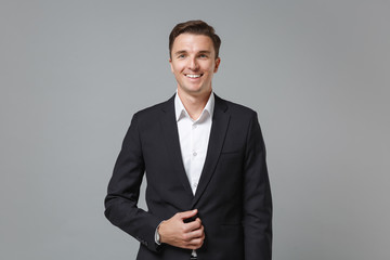Smiling successful young business man in classic black suit shirt posing isolated on grey background studio portrait. Achievement career wealth business concept. Mock up copy space. Looking camera.