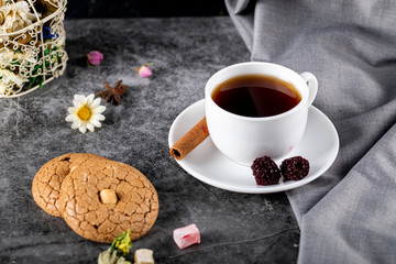 A white cup of tea with berries, cinnamon and cookies 