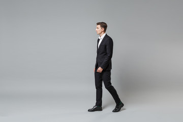 Side view of successful young business man in classic black suit shirt posing isolated on grey wall background in studio. Achievement career wealth business concept. Mock up copy space. Looking aside.