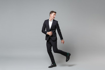 Fototapeta na wymiar Side view of funny young business man in classic black suit shirt posing isolated on grey background in studio. Achievement career wealth business concept. Mock up copy space. Looking aside, running.