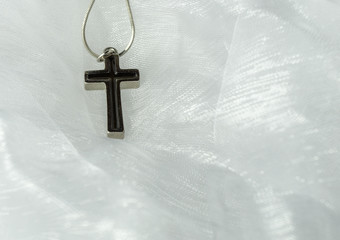 A silver cross with black inlet on a delicate white organza fabric