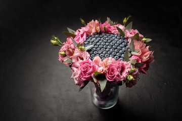 Unusual bouquet of blueberries framed around a circle of pink orchids and roses on a dark background