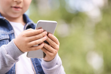 Young school boy texting outdoor. Male person using smartphone. Little hands with cell phone. Green bokeh street background.
