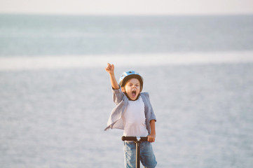 happy succeed little boy in sport helmet standing on sea background with scooter with hand up for success victory winner concept with copy space © ruslanshug