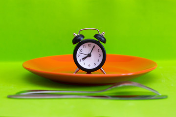 Clock on an empty plate, focus on the clock. Concept for the theme of weight loss. Diet, food ban...