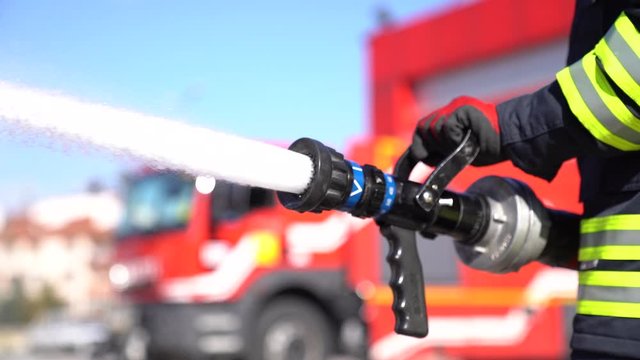 Firefighter is using fire hose  for training.  Fire engine and 	fire station  background. Close up shot.