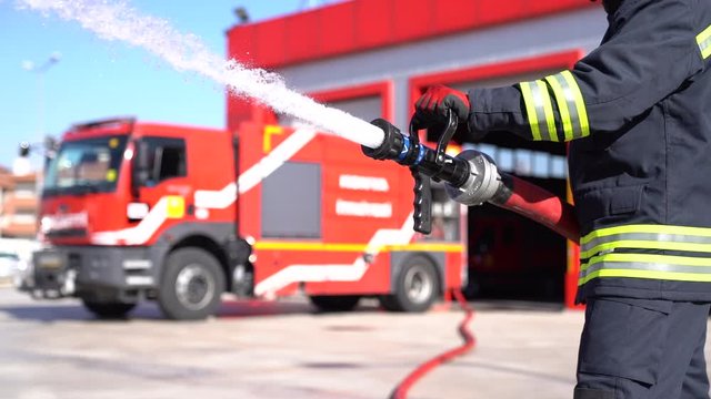 A fireman keeps fire hose and extinguishes fire for training. Fire station background.