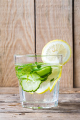 Healthy water with lemon and cucumber in a glass against wood background