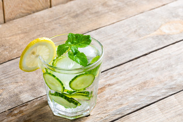 Healthy water with lemon and cucumber in a glass against wood background