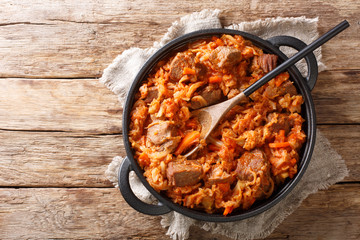 Braised Cabbage with meat, tomatoes, carrots and onions close-up in a pan. Horizontal top view
