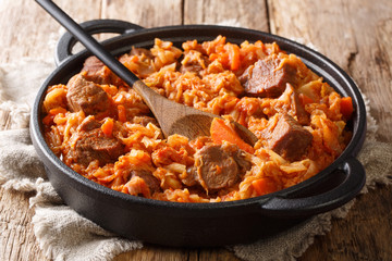 Braised Cabbage with meat, tomatoes, carrots and onions close-up in a pan. horizontal