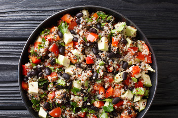 Dietary fitness salad of quinoa, avocado, pepper, tomatoes and black beans close-up in a plate. Horizontal top view