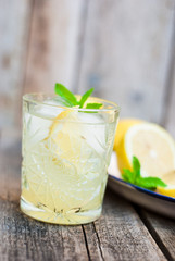 Glass with fresh lemonade on a wooden table with slices of lemon in the background