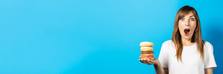 young girl holds four donuts on a palm on a blue background. Banner. The concept of diet, bright colors, emotions