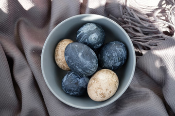 Easter background with Easter eggs and feathers in a ceramic gray bowl. Background with easter eggs. Naturally dyed eggs prepared for Easter on gray texture tablecloth background. Happy Easter