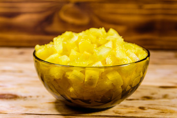 Glass bowl with chopped pineapple on wooden table