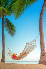 Young girl resting in a hammock under tall palm trees, tropical beach