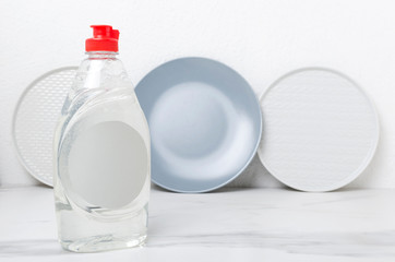Grey and white clean plates near the wall, bottle of liquid dishwasher detergent on the kitchen table.Empty space for text