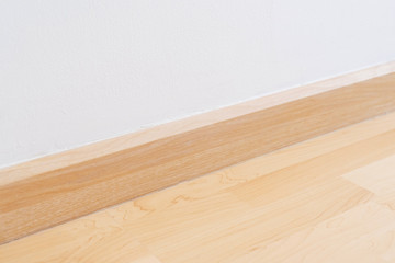 Wooden wall base skirting, finishing material with wood laminate floor and white mortar wall. Empty room with white wall and wooden floor.