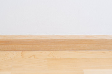 Wooden wall base skirting, finishing material with wood laminate floor and white mortar wall. Empty room with white wall and wooden floor.