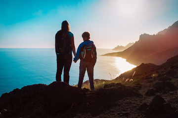 silhouette of mother and son travel at sunset mountains near sea