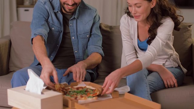 leisure, people and fast food concept - happy couple opening and eating takeaway pizza at home in evening