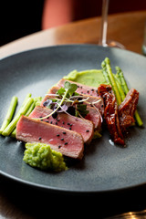 Close up of medium-rare tuna steak with broccoli puree and asparagus, served on minimalist black table