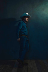 Man wearing denim shirt and cowboy hat standing against wall.