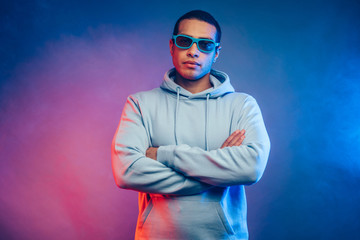 Calm peaceful and serious young arabian or egyptian man with crossed hands look straight on camera through sunglasses. Wear youth hoodie. Stand alone isolated over colorful background.