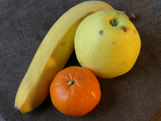 Fresh fruits, banana, orange and apple on the brown table
