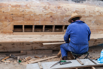 man with work overalls fixing a wooden boat