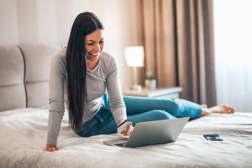 Girl sitting in the bedroom using laptop and credit card for online shopping.