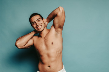 Cheerful hot sexy attractive young arabian man posing on camera topless. Hold hands in lock position behind head. Hips are coveres with white towel. Isolated over background.