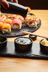 Hand  pouring soy sauce (Shoyu) from little jug into the bowl before eating japanese food such as sushi roll