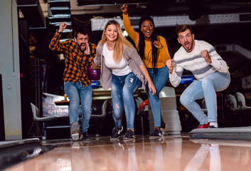 Group of friends enjoying time together laughing and cheering while bowling at club.